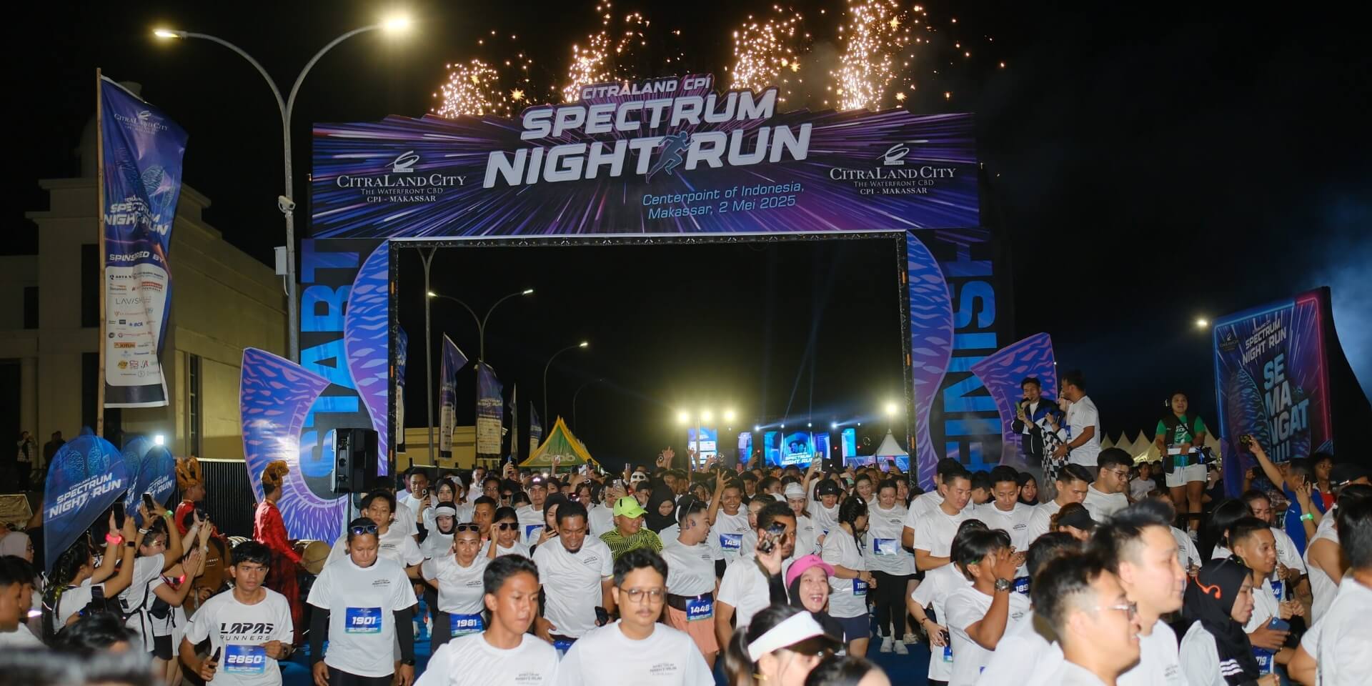 nighttime street race start with a crowded group of runners under a lit archway and fireworks   citraland city center point indonesia