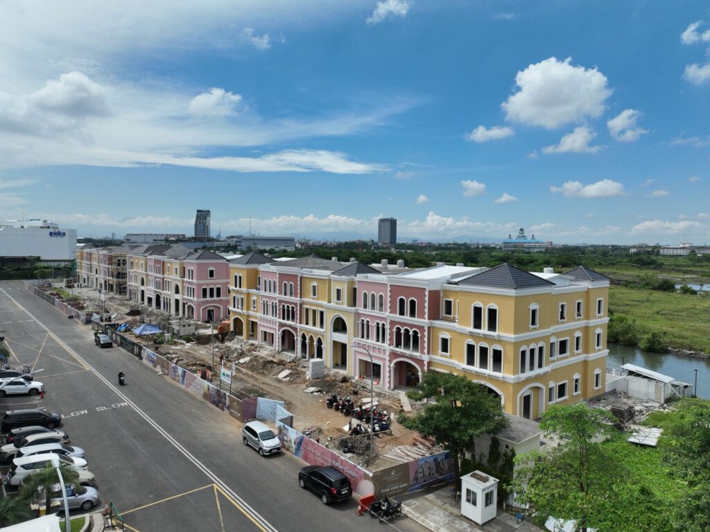 WhatsApp Image 2026-07-17 at 81445 AM - CitraLand City Center Point Indonesia row of pastel colored townhouses under construction along a busy street with a river on the right and a blue sky above citraland city center point indonesia